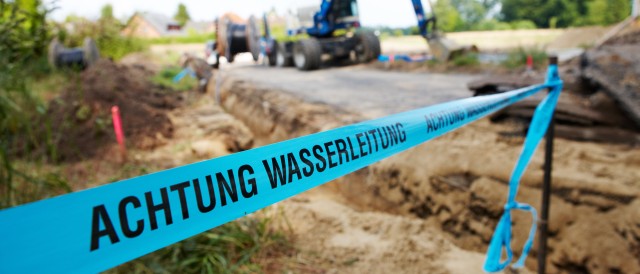 Blaues Flatterband mit der Aufschrift Achtung Wasserleitung vor einer Baustelle